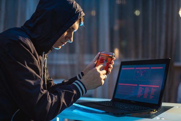 Hacker using smartphone to steal data from laptop.